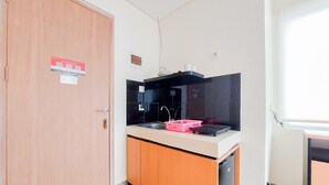 A compact kitchen with a wooden door, a sink, a black countertop, and a small refrigerator. - Homey And Comfort Studio Apartment At B Residence (Pagedangan)