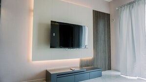 Ein modernes Wohnzimmer mit einem wandmontierten Flachbildfernseher, einer grauen Unterhaltungsecke und einem großen Fenster mit Vorhängen.