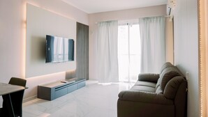 Ein modernes Wohnzimmer mit einem an der Wand montierten Flachbildfernseher, einer Couch, einem Esstisch mit Stühlen und einem großen Fenster mit Vorhängen.