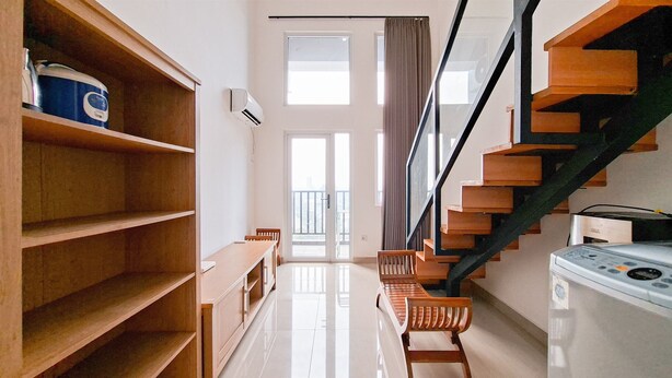 A spacious room with a wooden bookshelf, a bench, a washing machine, and a staircase. - Cozy Stay And Comfy Studio Loft Kingland Avenue Apartment (South Tangerang)