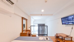 A hotel room with a bed, a desk, a chair, a TV, and a window with curtains. - Cozy Stay And Comfy Studio Loft Kingland Avenue Apartment (South Tangerang)