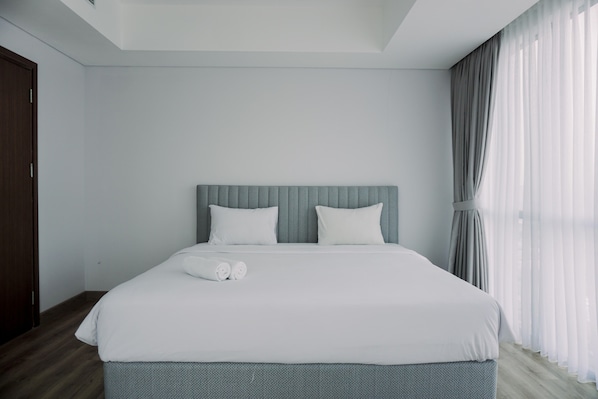 A modern hotel room with a large bed, a headboard, and a window with curtains.