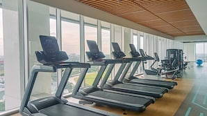 A gym with treadmills aligned against a wall of large windows, overlooking a cityscape. - Wonderful And Homey 1Br The Smith Alam Sutera Apartment (Tangerang)