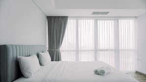 A modern hotel room with a large bed, a headboard, and a view of the city through sheer curtains. - Wonderful And Homey 1Br The Smith Alam Sutera Apartment (Tangerang)