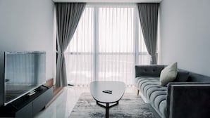 A modern living room with a flat-screen TV, a sofa, a coffee table, and a large window with sheer curtains. - Wonderful And Homey 1Br The Smith Alam Sutera Apartment (Tangerang)