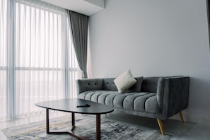 Un salon moderne avec un canapé gris, une table basse ronde et une grande fenêtre ornée de rideaux légers.