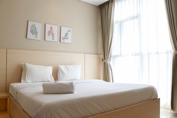 Una cama bien tendida con sábanas y almohadas blancas, un cabecero de madera y tres cuadros de pájaros colgados en la pared.