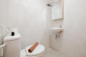 A small, clean bathroom with a toilet, sink, and a towel on the toilet. - Minimalist 1Br With Extra Room At Evenciio Margonda Apartment (Depok)