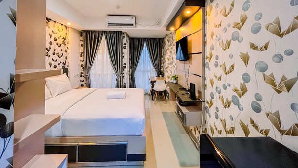 A hotel room with a bed, desk, chair, and a TV on the wall. - Simple And Cozy Studio Tamansari Skylounge Makassar Apartment (Makassar)