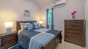 A bedroom with a bed, nightstands, a dresser, an air conditioner, and a window with curtains. - Modern, stylish, peaceful apartment with a great view! (Buckleys)