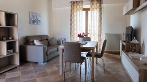 A living room with a sofa, a dining table with chairs, a TV, and a radiator.