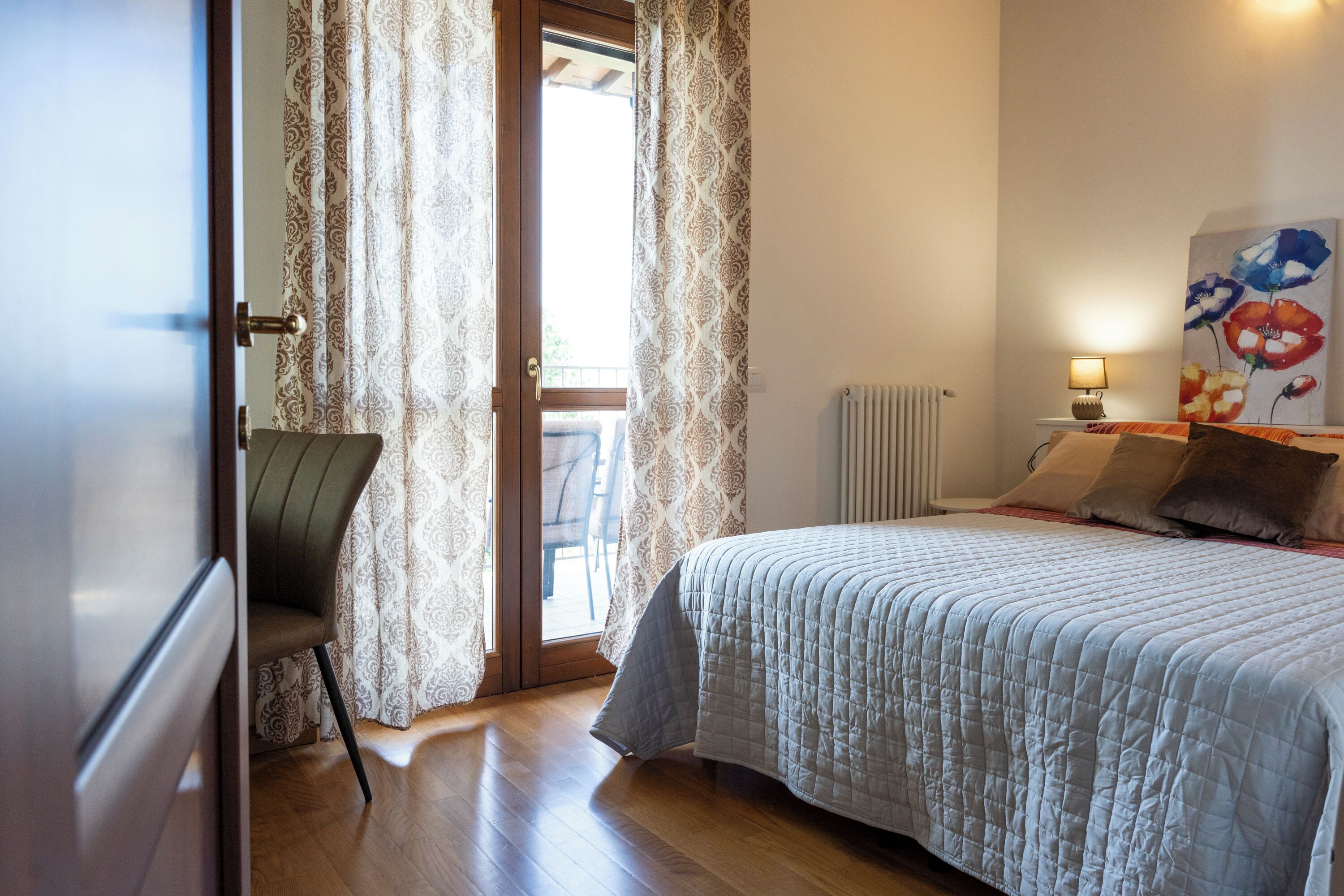 A bedroom with a bed, a chair, a radiator, and a painting on the wall.