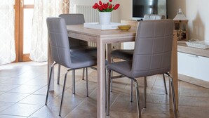 A dining area with a wooden table, four grey chairs, a TV, and a vase with red flowers.