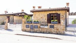 A stone building with a tiled roof, a gated entrance, and potted plants on the balcony.