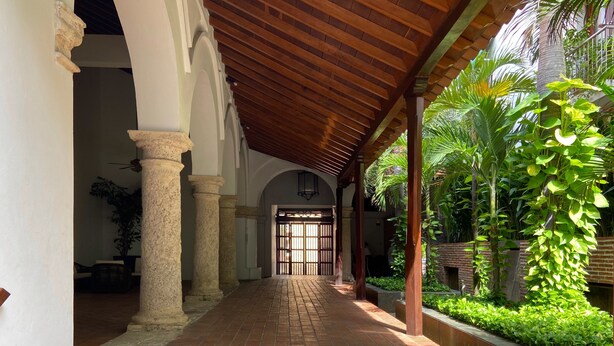 A covered corridor with brick flooring, columns, and a view of a gate leading to a courtyard with greenery. - Wynwood Eslava in Cartagena (Cartagena)