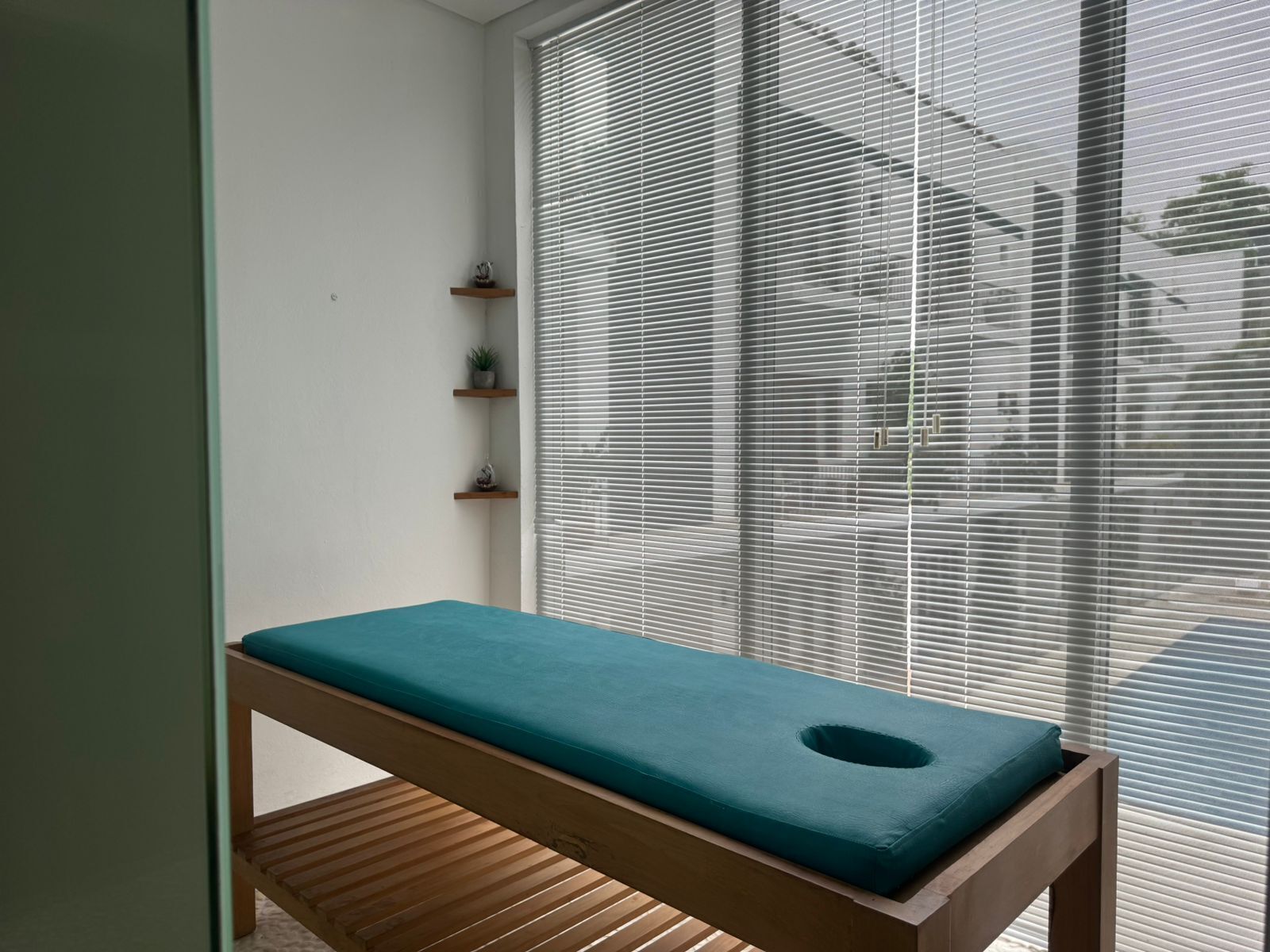 Ein Zimmer mit einer hölzernen Sitzbank, einem türkisblauen Kissen und einem Fenster mit Jalousien.