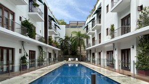 A swimming pool with lounge chairs, surrounded by white buildings with balconies and greenery. - Wynwood Eslava in Cartagena (Cartagena)
