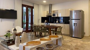 A modern kitchen with stainless steel appliances, a dining area with a glass table, and a TV mounted on the wall. - Wynwood Eslava in Cartagena (Cartagena)