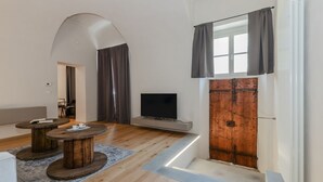 A modern living room with a flat-screen TV, wooden coffee tables, a patterned rug, and a rustic wooden door.