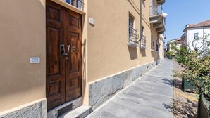 A narrow street with a wooden door, a stone-paved path, and a building with a balcony.