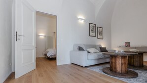 A modern living room with a white sofa, a wooden coffee table, and a radiator in the background.