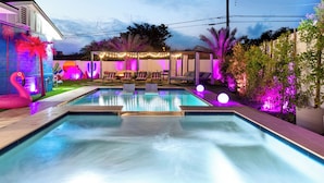 Ein Schwimmbecken mit Wasserspiel, umgeben von einer Terrasse mit Liegestühlen und Lichterketten.