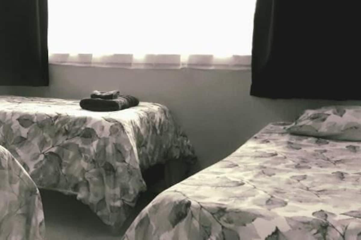 A room with three beds, each with a floral-patterned bedspread. There is a small table and a chair in the room.