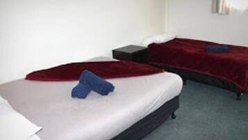 Habitación de hotel con dos camas, cada una con una manta roja y un cojín. Hay una mesita de noche pequeña entre las camas.