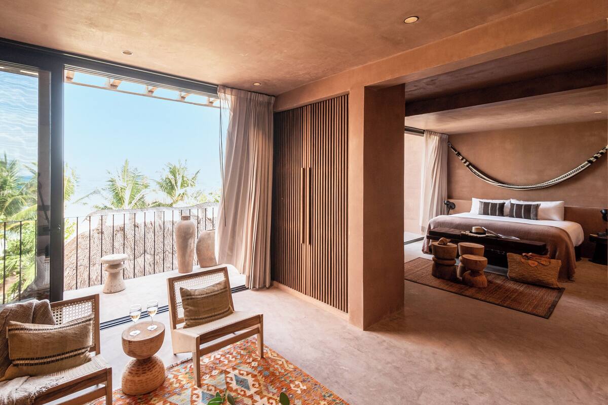 A modern bedroom with a large window, a bed with a headboard, and a seating area with a patterned rug.