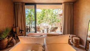 Een slaapkamer met een groot bed, uitzicht op de buitenruimte, en een balkon met stoelen en planten.