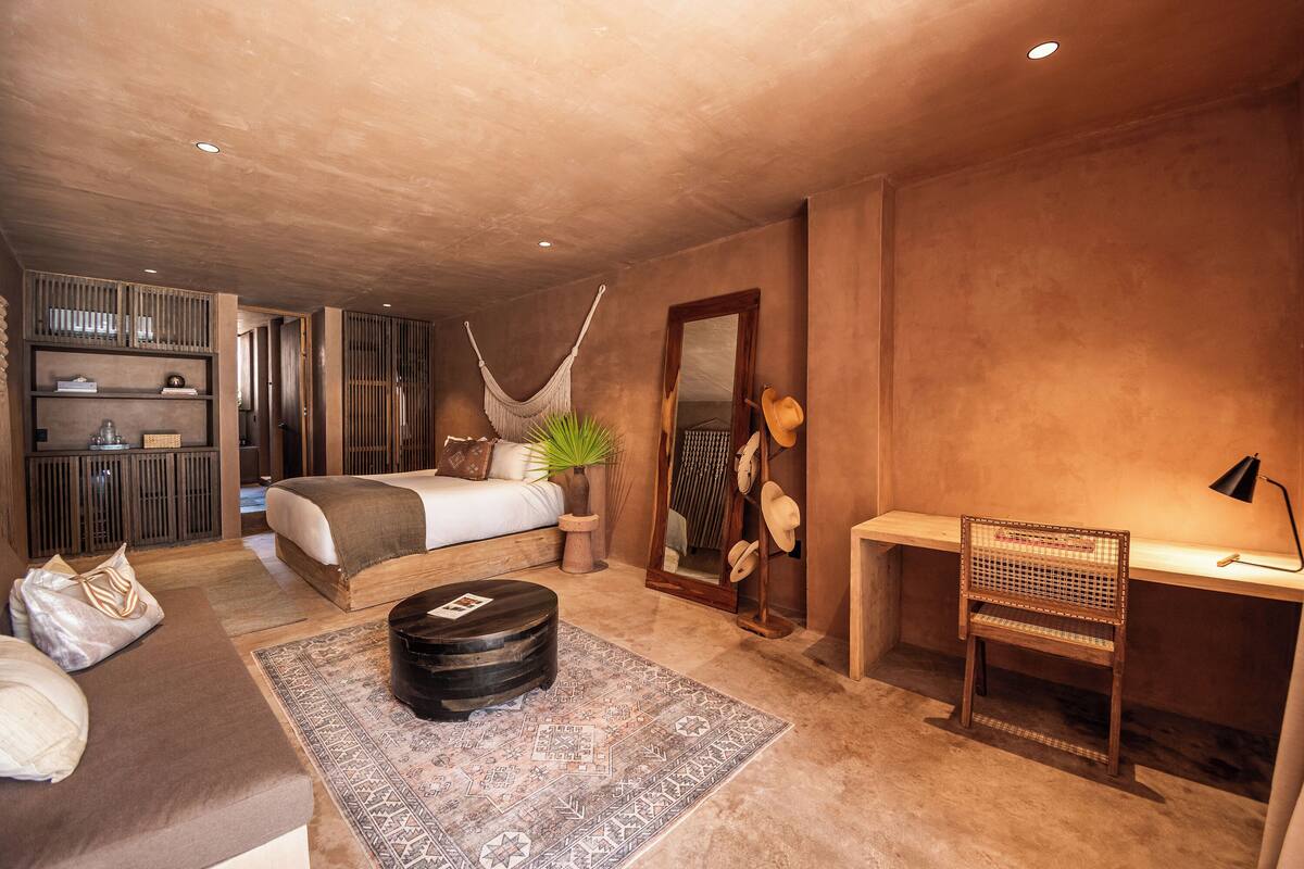 A bedroom with a bed, bedside table, chair, desk, and a hammock.