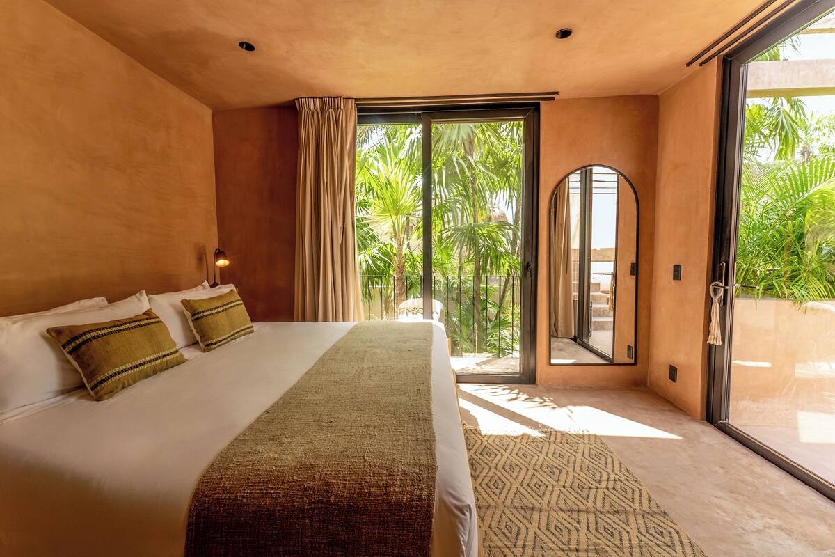 A bedroom with a large bed, a view of palm trees through a glass door, and a patterned rug.
