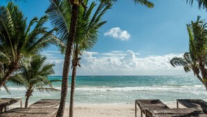 A beach with thatched umbrellas and palm trees. - Xela Tulum, a Member of Design Hotels (Tulum)