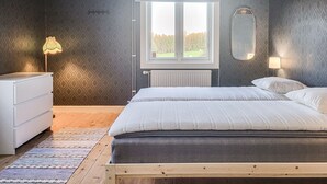Un dormitorio con cama, cómoda, ventana y radiador.