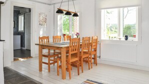 Un área de comedor con una mesa y sillas de madera, una lámpara colgante y una ventana con vistas a zonas verdes.