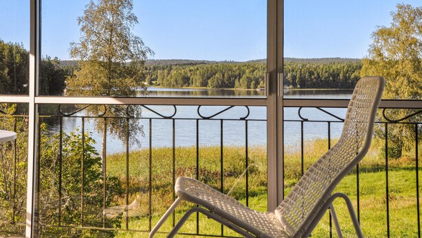 Un balcón con una silla de mimbre, con vistas a un lago y una zona boscosa.