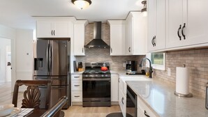 A modern kitchen with white cabinets, stainless steel appliances, and a brick backsplash. - Meadow Farm in Holly Springs, NC (Holly Springs)