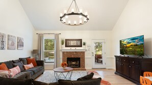 A living room with a fireplace, sofa, television, and artwork on the walls. - Meadow Farm in Holly Springs, NC (Holly Springs)