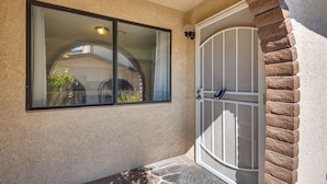 A house entrance with a stone-paved entrance, a glass door with a metal handle, and a window with a black frame.