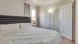 A bedroom with a bed, curtains, a nightstand, a lamp, and a door.