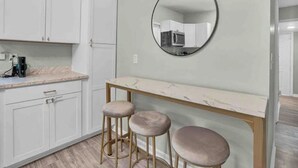 Une cuisine avec des meubles blancs, un plan de travail en marbre et un miroir rond. On y trouve trois tabourets placés sous le plan de travail.