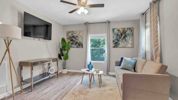 Un salon comprenant un canapé, une table basse, un téléviseur fixé au mur et un ventilateur de plafond.