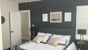 A bedroom with a bed, a ceiling fan, a door, and framed pictures on the wall.