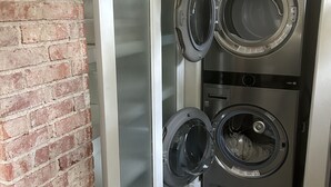 A laundry room with two stacked front-loading washing machines and a brick wall.