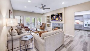 A spacious living room with a fireplace, a ceiling fan, and a view of the kitchen. - Sonrisa Sunshine-Pool,Spa,Walk to BNP 3BD #066685 (La Quinta)