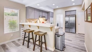 A modern kitchen with a central island, bar stools, a stainless steel refrigerator, and a trash can. - Sonrisa Sunshine-Pool,Spa,Walk to BNP 3BD #066685 (La Quinta)