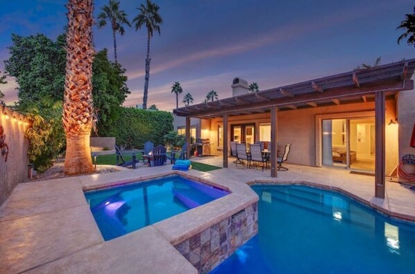A swimming pool with a stone border, a covered patio area, and a view of a house with a pergola.