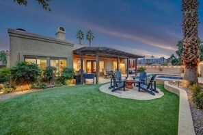 A modern house with a covered patio, a swimming pool, and a well-maintained lawn.
