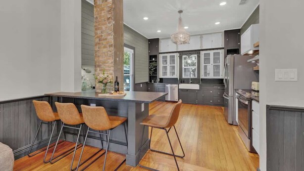 A modern kitchen with a central island, bar stools, and a brick accent wall. - Historic Gem Near Schlitterbahn (New Braunfels)