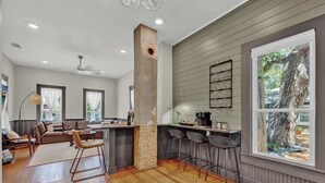 A modern kitchen with a central island, bar stools, and a large window with a tree view. - Historic Gem Near Schlitterbahn (New Braunfels)